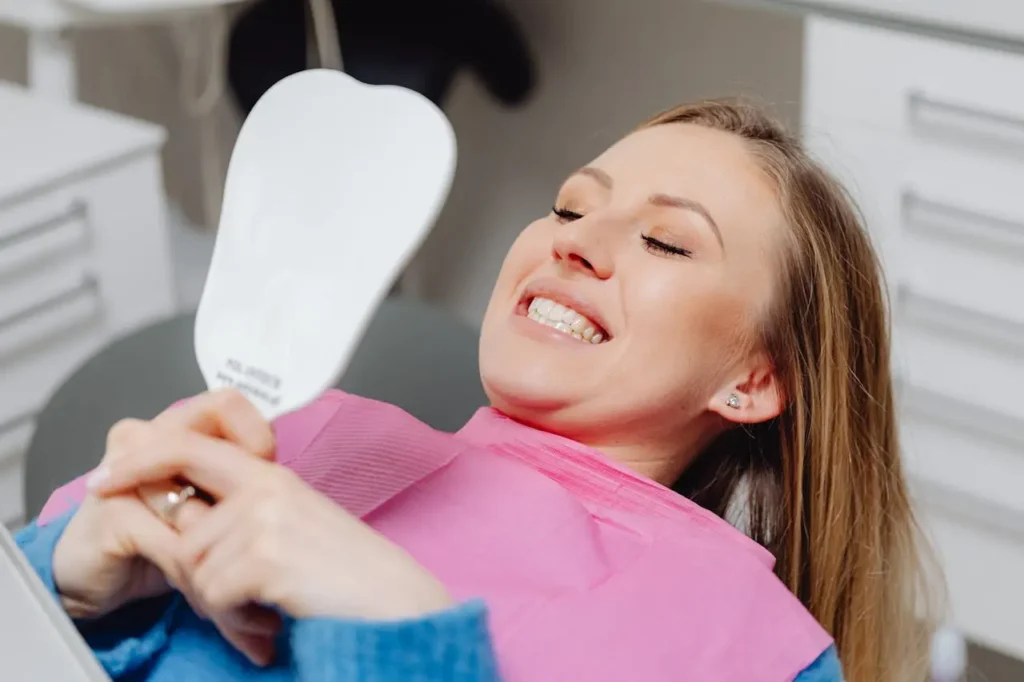 Donna che osserva allo specchio il suo sorriso dopo un trattamento di estetica dentale finalizzato a migliorare l’equilibrio tra denti, gengive e labbra.
